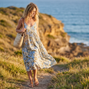 Woman in a floral midi dress, flat sandals and straw bag walking along a coastal path in spring