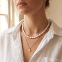 Woman wearing three layered gold necklaces: a short chain, a pearl strand and a long pendant necklace