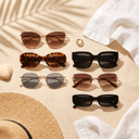 Six pairs of women's sunglasses in different frame shapes on linen with a straw hat and a seashell