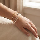 Wrist wearing a stack of gold bracelets: hammered bangle, paperclip chain, zircon tennis bracelet and pearl bracelet
