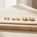 Gold stud earrings, zircon huggie hoops and chunky gold hoop earrings side by side on cream linen
