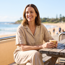 Woman in a sand linen two-piece set with layered gold necklaces at a seaside cafe