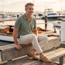 Man in a sage knit polo shirt, stone chinos and suede loafers by the harbour
