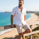 Man in a white linen shirt with a silver chain necklace and bracelets at a beach lookout